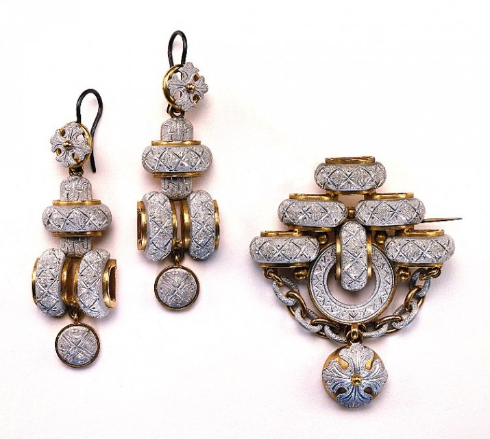 Museum photograph of a circa-1860 French brooch and pair of earrings made from bright-cut engraved aluminium with gold mounts